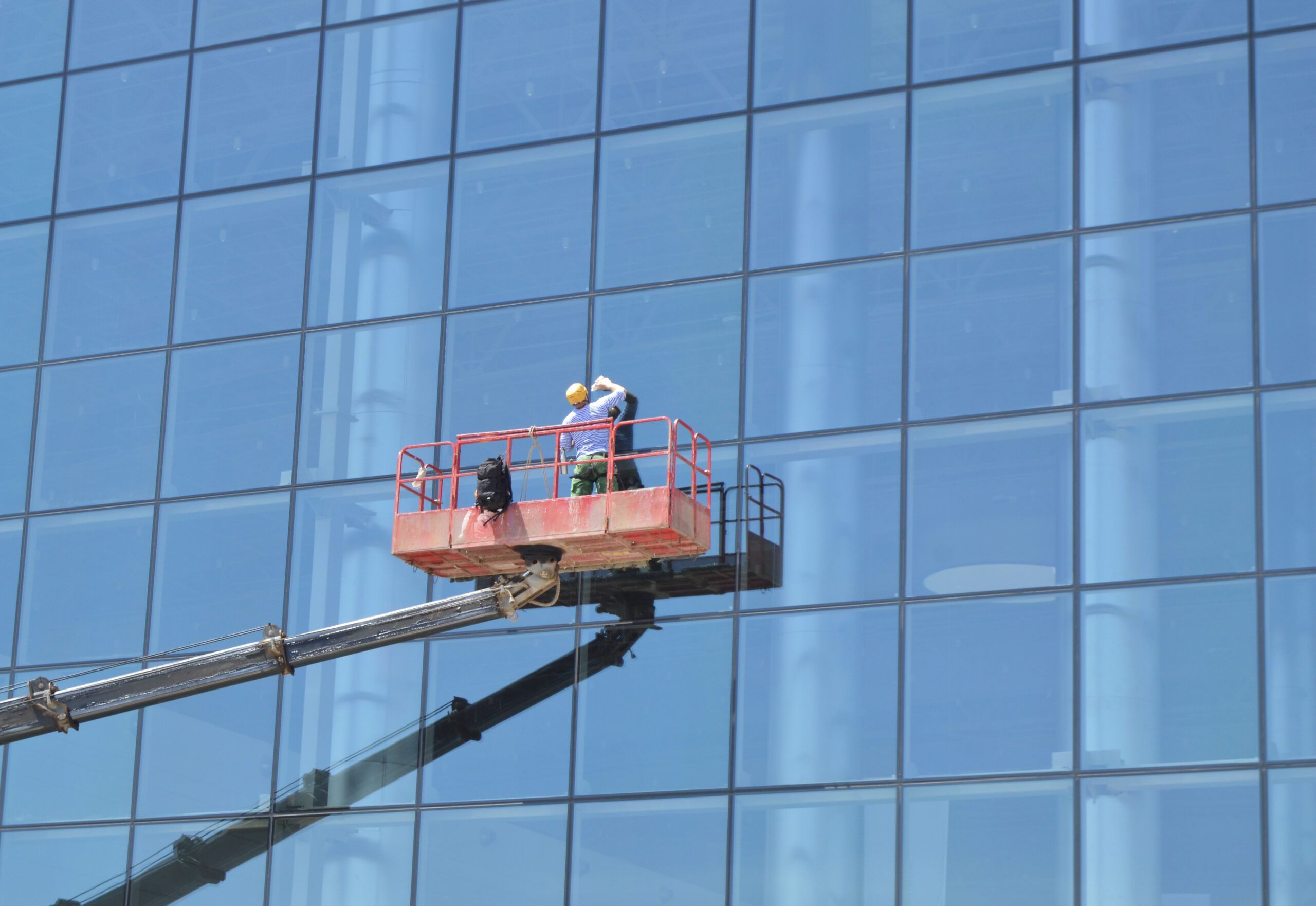 Worker washes the Windows on the glass facade of a skyscraper, standing on the platform of a crane